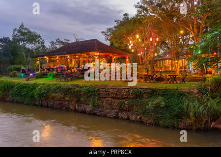 Scène soirée illuminée avec restaurant en plein air au bord de la rivière dans la jungle tropicale, PAI, Thaïlande Banque D'Images