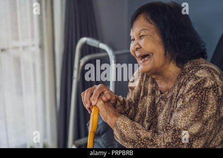 Senior woman laughing et tenant la canne en bois dans la salle de séjour à la maison Banque D'Images