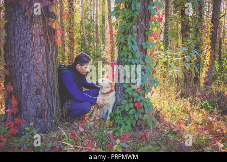 Un homme avec le Labrador retriever dog balade dans la forêt de pins à l'automne. L'homme et le chien assis entre deux arbres Banque D'Images