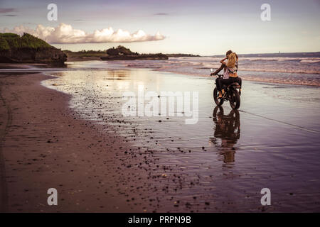 Vue arrière du couple riding sur la plage de l'océan de sable au matin Banque D'Images