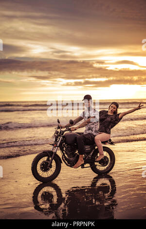 Heureux couple riding on seashore pendant le lever du soleil Banque D'Images