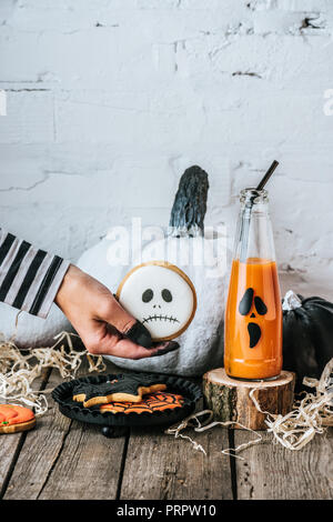 Cropped shot of woman holding cookie halloween près de citrouilles et jus sur la surface en bois Banque D'Images
