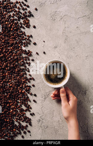 Cropped shot of woman holding tasse de café sur une surface en béton, avec des grains de café renversé Banque D'Images
