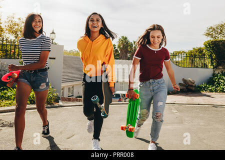 Trois jeunes filles exerçant son longboard skateboards et la marche à l'extérieur par une journée ensoleillée. Cheerful young girls jouent dehors dans la rue. Banque D'Images