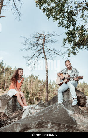 Petit ami barbu romantique jouant de sa guitare tandis que les dépenses dans les montagnes, Banque D'Images
