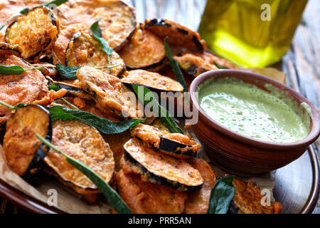 Aubergine aubergine frite pané tranches sur une plaque de faïence avec du yaourt persil trempant dans un bol d'argile sur une table rustique avec des ingrédients à la Banque D'Images