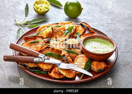 Aubergine aubergine frite pané tranches sur une plaque de faïence avec du yaourt persil trempant dans un bol d'argile sur une table en béton avec des ingrédients à t Banque D'Images