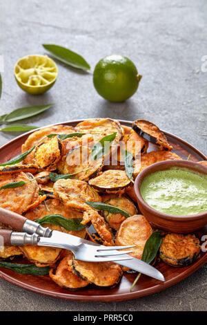 Aubergine aubergine frite pané tranches sur une plaque de faïence avec du yaourt persil trempant dans un bol d'argile sur une table en béton avec de la chaux et à la sauge Banque D'Images