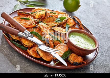 Aubergine Aubergine croustillant pané tranches sur une plaque de faïence avec du yaourt persil trempant dans un bol d'argile sur une table en béton avec des ingrédients à Banque D'Images