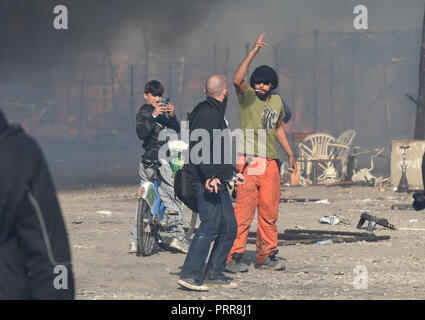 26 octobre 2016 - Calais, France : Un activiste (pantalon orange) menace d'empêcher les journalistes médias d'entrer dans la 'jungle' De Calais camp de migrants comme énormes incendies éclatent dans plusieurs endroits dans le campement. Demantelement de la jungle de Calais, l'un des plus grands camps de migrants au monde. *** FRANCE / PAS DE VENTES DE MÉDIAS FRANÇAIS *** Banque D'Images