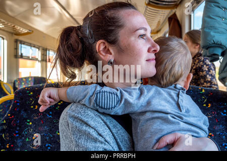 Young happy mother holding baby alors qu'il tire ses cheveux tout en voyageant par train Banque D'Images