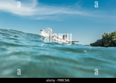 Jeune homme sportif natation sur le surf de l'océan en bord de plage de Nusa Dua, Bali, Indonésie Banque D'Images