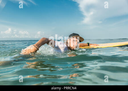 Homme concentré de natation avec surfeur surf board à l'océan sur la plage de Nusa Dua, Bali, Indonésie Banque D'Images