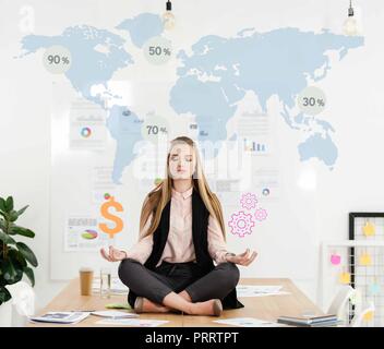 Calme businesswoman sitting in lotus position sur table avec le signe du dollar et cogs dans les mains et l'arrière-plan sur la carte du monde Banque D'Images