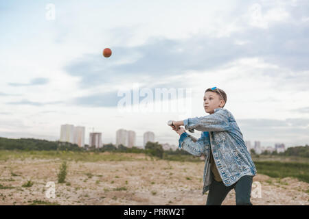 Veste en jean garçon en jouant avec batte de baseball et balle à jour nuageux Banque D'Images