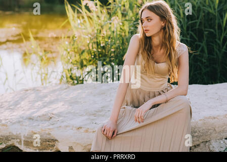 Élégant belle jeune femme assise sur le sol près du lac Banque D'Images