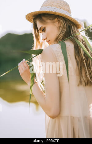 Belle blonde jeune femme en chapeau de paille posant près du lac Banque D'Images