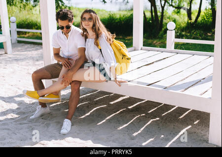 Jeune couple assis sur le banc en bois à sandy city beach Banque D'Images