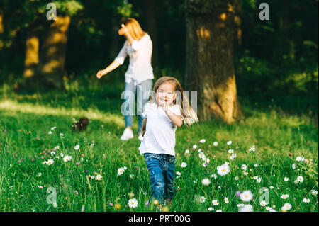 Portrait of smiling kid fonctionnant avec la mère se tenant derrière en forêt Banque D'Images