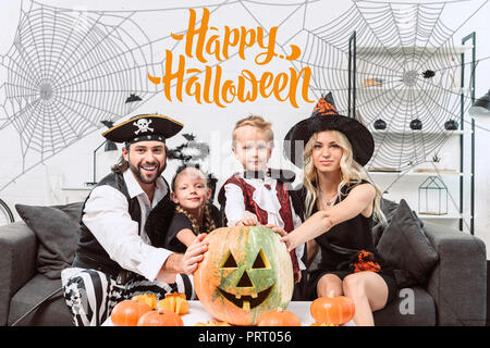 Portrait de famille dans divers costumes de Halloween à table de café à la maison avec des citrouilles avec 'happy Halloween lettrage' Banque D'Images