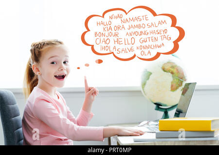 Écolier rousse étudie avec livres et ordinateur portable et pointant vers le haut sur les mots de différentes langues dans bulle Banque D'Images