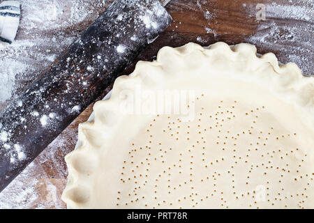 Le beurre fait maison pâte à tarte dans l'assiette à tarte avec bord pincé à cannelures, rouleau à pâtisserie et un boule de pâte farinée sur fond de bois rustique. A croûte Banque D'Images