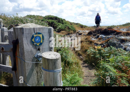 Femme seule marche randonneur passé porte en bois et panneau pour l'île d'Anglesey Sentier Littoral près du village de pêcheurs de Cemaes, Pays de Galles, Royaume-Uni. Banque D'Images