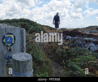 Homme seul marche randonneur passé porte en bois et panneau pour l'île d'Anglesey Sentier Littoral près du village de pêcheurs de Cemaes, Pays de Galles, Royaume-Uni. Banque D'Images