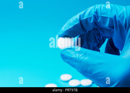 Une main gantée tient un comprimé blanc sur un fond bleu. Au laboratoire du centre médical. Banque D'Images