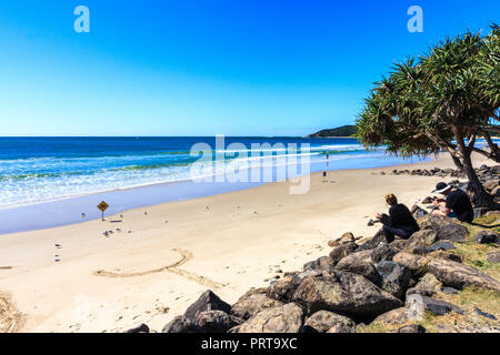 Byron Bay, Australie - 14 mai 2015 : Des gens assis sur des pierres sur la plage. La région est populaire auprès des jeunes. Banque D'Images