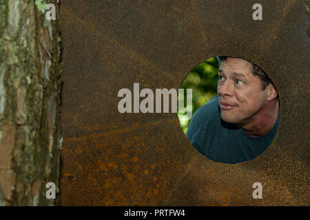 Vue de face des hommes à travers la plaque de fer dans le trou. Surpris homme heureux de faire le trou dans la plaque de fer. Cute woman regarder à travers le trou. Copy space Banque D'Images