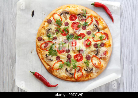 Des pizzas fraîches avec tomates, fromage, salami et champignons, décoré avec les feuilles de persil sur le morceau de papier cuisson. Vue d'en haut Banque D'Images