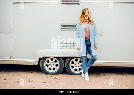 Femme élégante avec de longs cheveux blonds portant des lunettes appuyé contre bus, portrait Banque D'Images