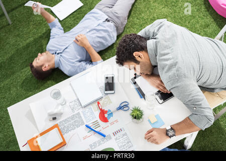 Les jeunes hommes d'dormir sur la table et tapis d'herbe verte à l'équipe d'affaires, bureau moderne Banque D'Images