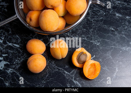 Organique mûres les abricots dans une passoire en acier. Composition dans un style rustique - jaune bio abricots juteux dans son ensemble et passoire en acier et des moitiés d'abricots o Banque D'Images