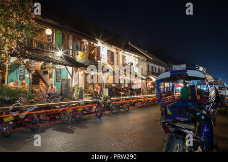 Des scooters, des taxis à trois roues (jumbo ou tuk-tuk) et peu de touristes dans un cadre idyllique des cafés dans les bâtiments de l'époque coloniale française à Luang Prabang, Laos, au crépuscule. Banque D'Images