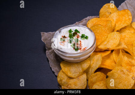 Croustilles de pommes de terre avec une trempette sur le papier parchemin. Noir foncé sur fond de table en pierre Banque D'Images