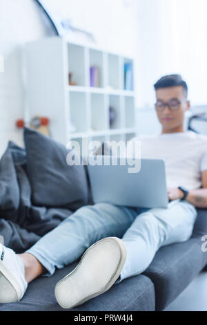 Focus sélectif de handsome asian man using laptop on sofa at home Banque D'Images