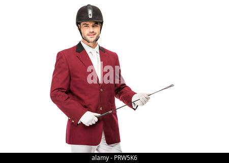Jeune cavalier souriant en uniforme holding horseman stick and looking at camera isolated on white Banque D'Images