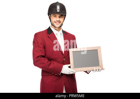 Heureux jeune cavalier en uniforme holding blank chalkboard and looking at camera isolated on white Banque D'Images