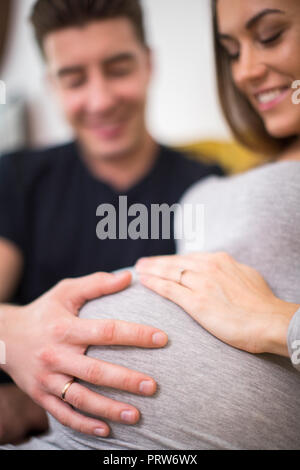 Pregnant Couple Sitting on Sofa avec l'homme de toucher l'estomac de womans Banque D'Images