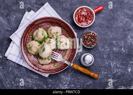 Khinkali boulettes géorgien avec de la viande, l'oignon vert et de la sauce tomate. Servi sur une plaque en céramique marron avec bol de sauce, mélanger le poivre et sel. Dark concr Banque D'Images