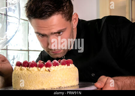 Beau vêtu de noir Baker Baker's coat met la touche finale à la Crème de framboise cake on cake stand Banque D'Images