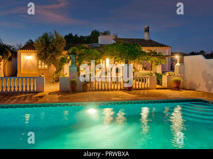 Une ancienne maison algarve rustique avec piscine et terrasse couverte de vigne au crépuscule, Portugal Banque D'Images