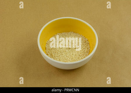 Blanc brut de graines de sésame dans le petit bol de condiment jaune et blanc Banque D'Images