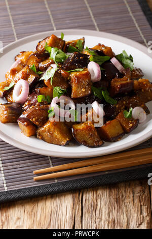 Aubergines du Sichuan dans une sauce épicée décorées avec des oignons et de la coriandre gros plan sur une plaque verticale sur la table. Banque D'Images