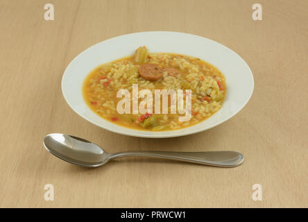 Saucisse gumbo de poulet soupe avec du riz et des légumes dans la soupe bol blanc avec de grandes cuillère à soupe sur table en bois Banque D'Images