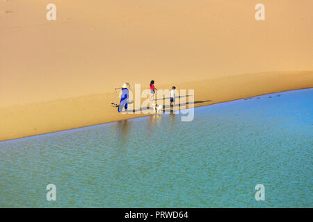 Femme porte une armature en bambou sur l'épaule et deux enfants à la maison à travers les dunes de sable de Mui Dinh Ninh Thuan Province Banque D'Images