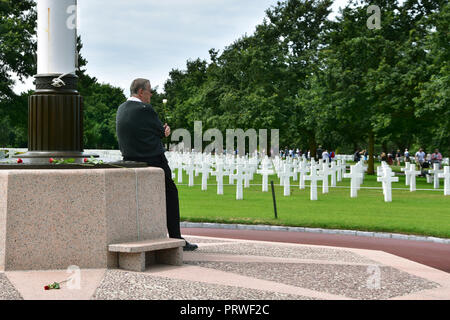 Omaha Beach, France - 17 juillet 2018 : homme âgé avec rose blanche devant les lignes infinies de pierres de tête en marbre blanc sur les prairies vertes Banque D'Images