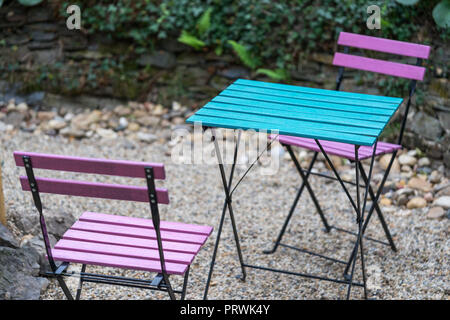 Deux chaises pliantes en bois de rose et d'un carré tableau bleu sont debout sur le gravier dans l'arrière-cour d'un café à la lumière naturelle dans la soirée Banque D'Images